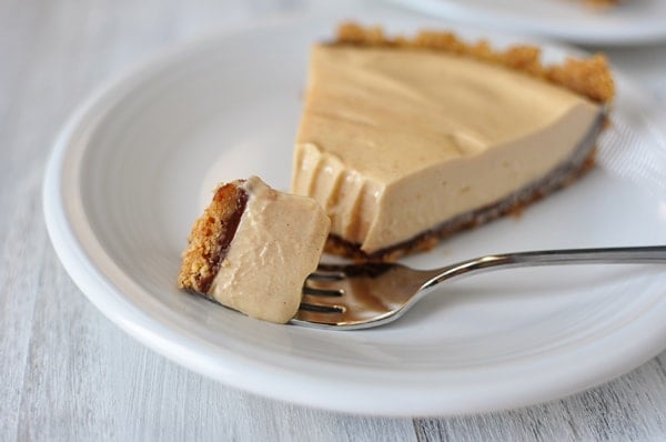 A slice of peanut butter pie on a white plate with a bite being taken out with a fork.