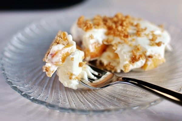Peach and cream dessert with a fork that takes a bite on a glass plate