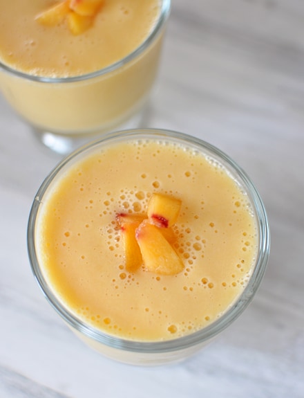 top view of a peach-orange smoothie in a glass goblet with a few peach dices