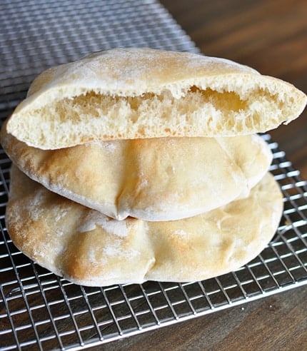 Three puffed pita breads stacked on a cooling rack with the top one split in half. 