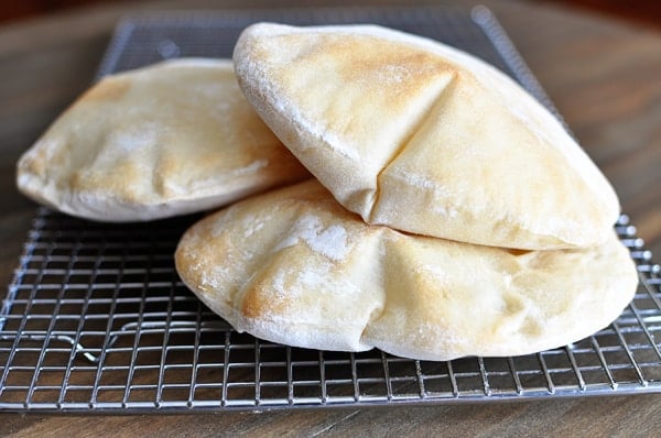 Three puffed homemade pita breads on a cooling rack. 