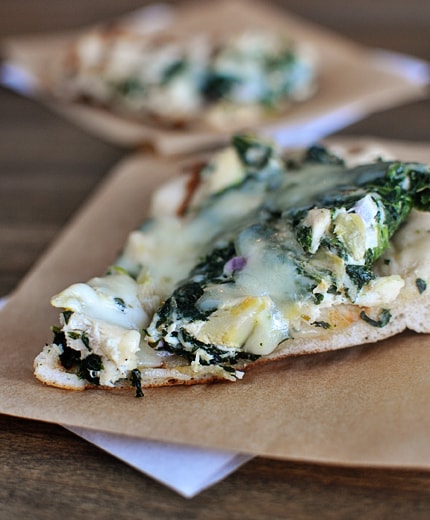 A slice of spinach artichoke pizza on a piece of parchment paper.