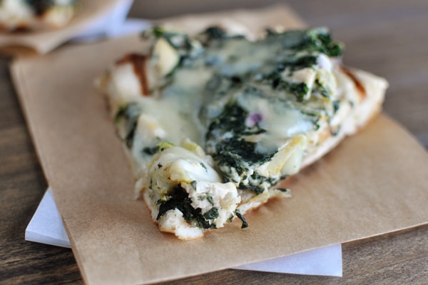 A slice of spinach artichoke pizza on a piece of brown parchment paper.