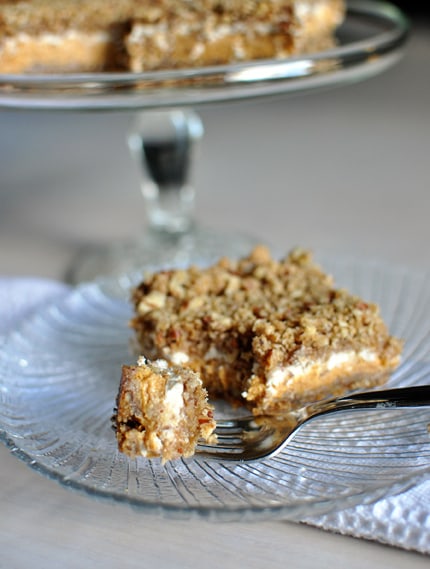 A glass plate with a pumpkin cheesecake crumble bars on it and a fork taking a bite out.