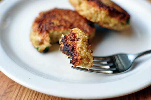 White plate with golden brown cooked quinoa patties with a fork taking a bite out.