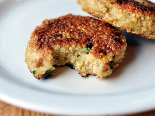 Golden brown cooked quinoa patty on a white plate with a bite taken out.