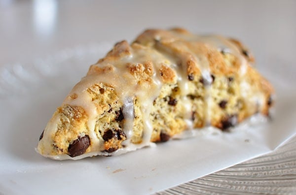 A glazed chocolate chip scone on a piece of parchment paper.