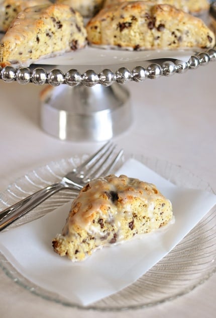 Raised serving platter with glazed chocolate chip scones and one scone on a plate below the platter.