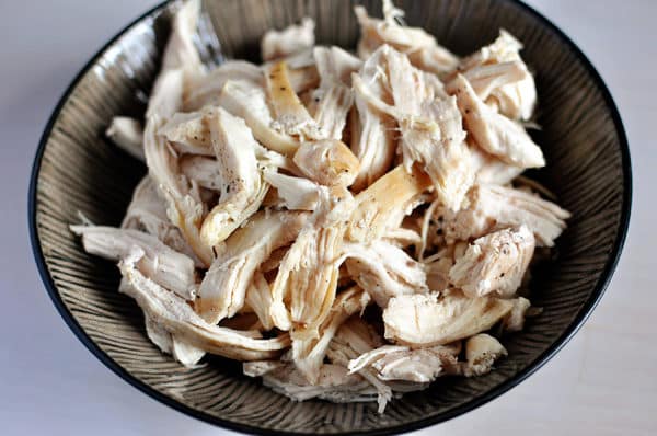 Cooked shredded, salted and peppered chicken, in a large ceramic bowl. 