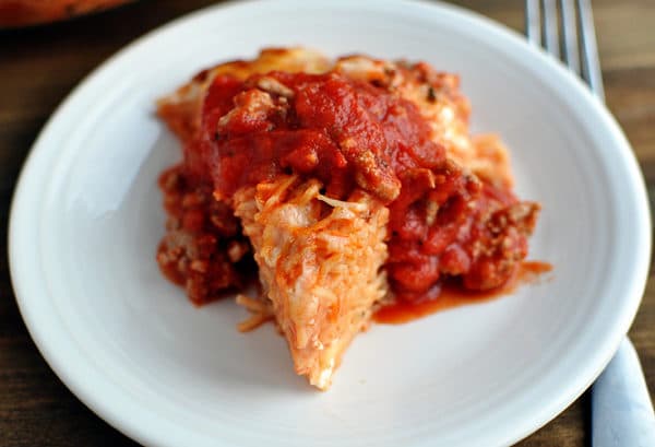 A triangle shaped serving of cooked spaghetti pie topped with red spaghetti sauce.