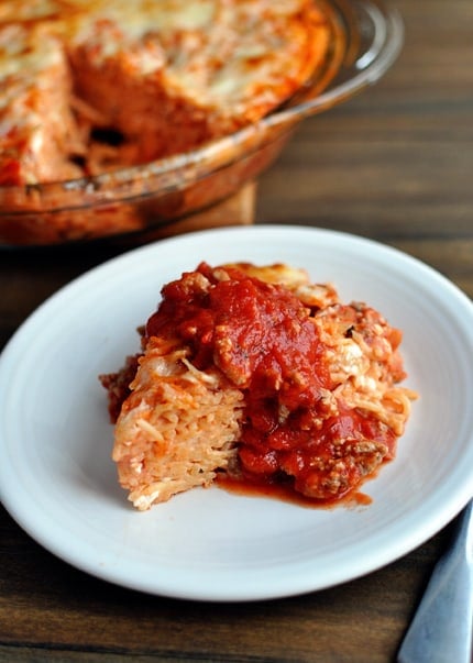 A white plate with a triangle of spaghetti pie covered in red spaghetti sauce.