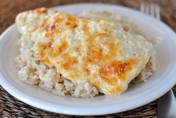 cheesy baked chicken breast over cooked rice on a white plate