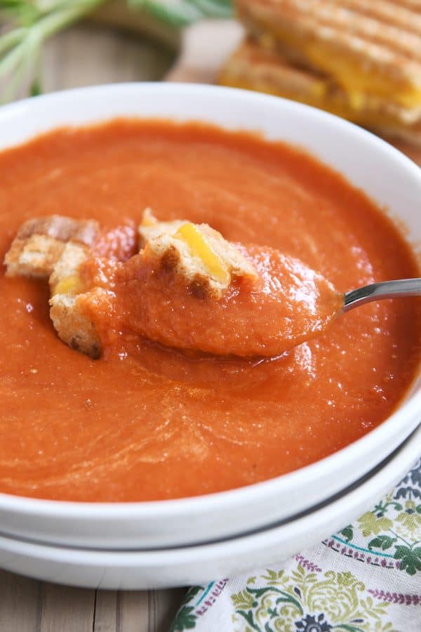 Spoonful of classic tomato soup in white bowl with grilled cheese croutons.
