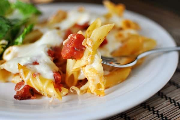 White plate with baked cheesy pasta and tomato dices.