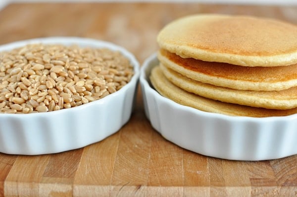 Two white ramekins with one filled with wheat berries and the other with stacked pancakes.