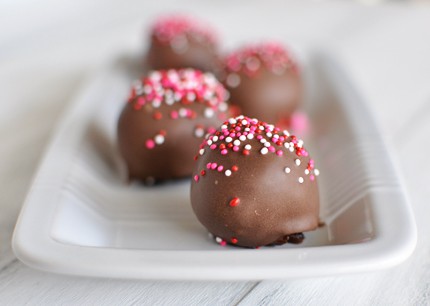 Chocolate dipped and sprinkle topped brownie truffles on a white dish.