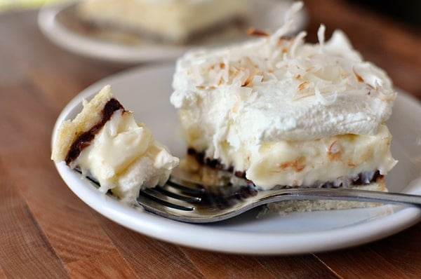 A layered coconut cream pie bar with a bite taken out on a white plate.