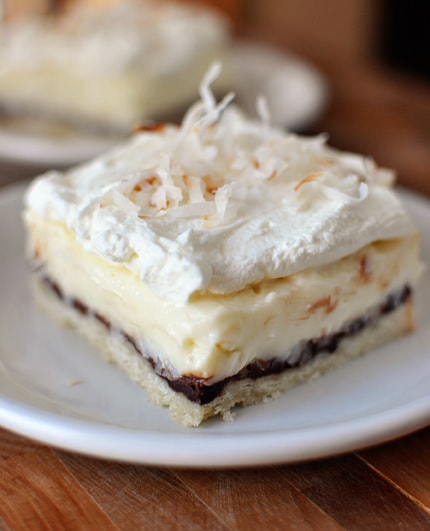 A square of layered coconut cream and chocolate pie bar with whipped topping and coconut on top.