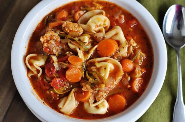 Top view of a sausage tortellini and veggie soup in a white bowl.