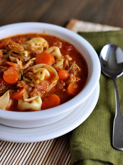 a white bowl with tortellini, sausage and veggie soup