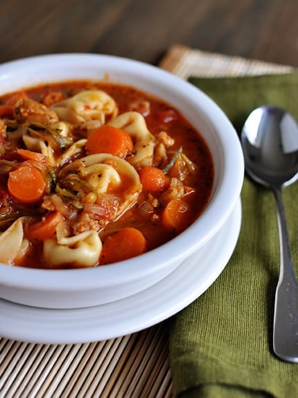 A white bowl with tortellini, sausage and veggie soup.