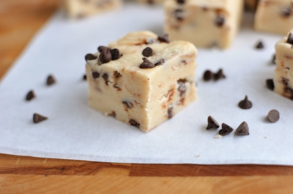 Squares of chocolate chip fudge on a sheet of parchment.