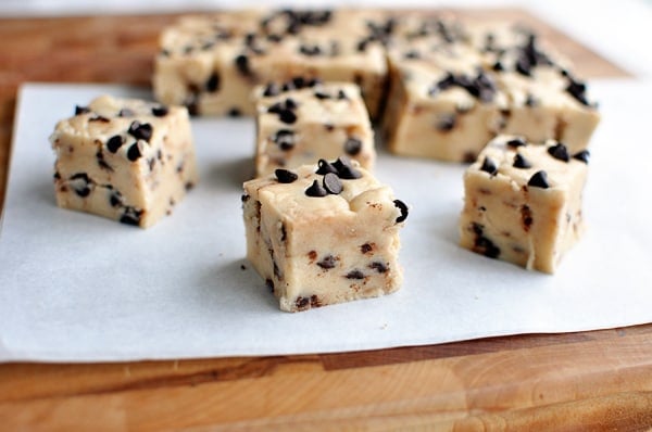 Small squares of chocolate chip fudge cut off a full slab on a sheet of parchment.