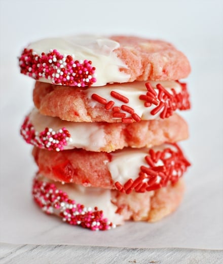 A stack of cherry shortbread cookies half dipped in white chocolate and sprinkles.