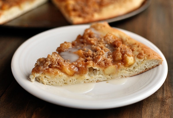A slice of apple cinnamon dessert pizza drizzled with glaze on a white plate.