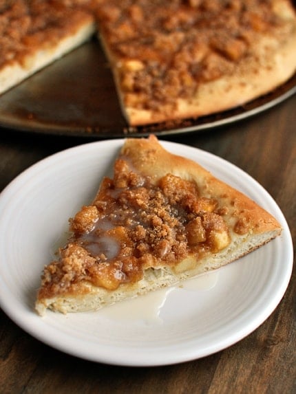 A slice of cinnamon apple streusel dessert pizza in front of the rest of the pizza.