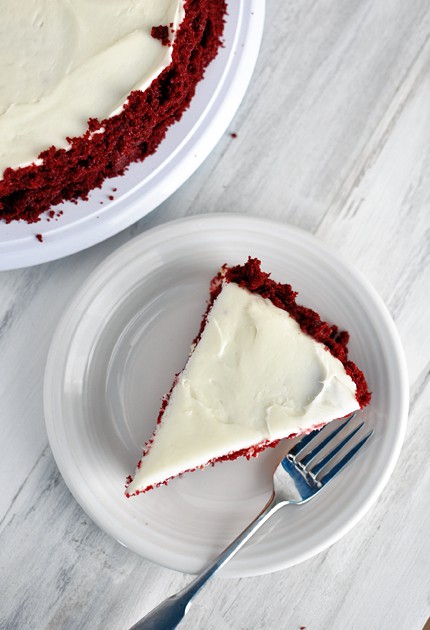Top view of a frosted piece of red velvet cake on a white plate.