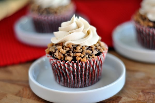 A toffee and frosting topped chocolate cupcake in a small white dish.
