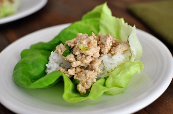 A large lettuce leaf filled with asian chicken and white rice on a white plate.