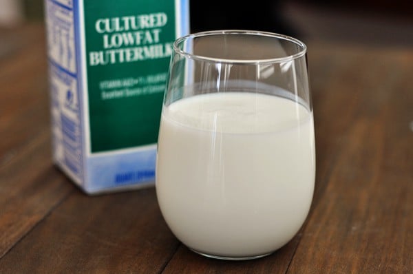 a clear glass of buttermilk with a carton of buttermilk behind it