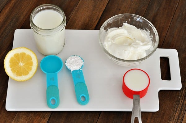 measuring spoons, lemon, milk, and sour cream on a white cutting board