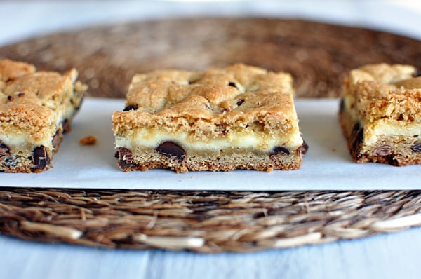 Three chocolate chip bars with a cheesecake middle lined up on a sheet of parchment paper.