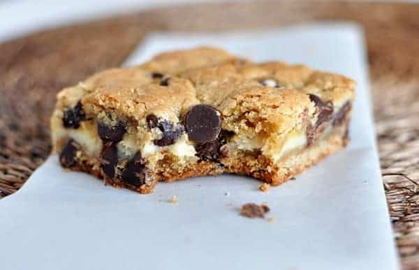 A cheesecake filled chocolate chip bar with a bite taken out on a white piece of parchment.