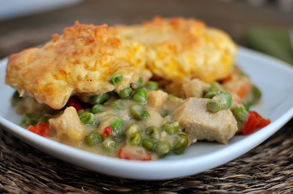 A plate of chicken and veggie mixture with a cooked cheddar biscuit topping.