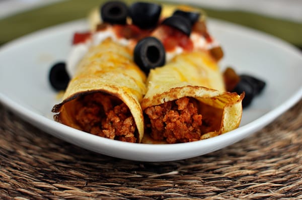 White plate with two cornmeal enchilada filled crepes topped with black olives, salsa, and sour cream.