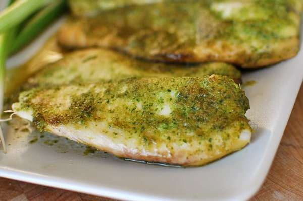 Baked tilapia with green sauce and herbs on top of each fillet.