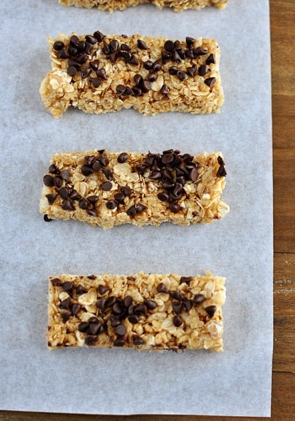 Top view of homemade granola bars topped with chocolate chips cut into rectangles on a piece of parchment paper.