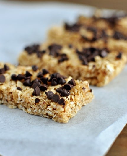 Homemade granola bars with chocolate chips sprinkled on top lined up on a piece of parchment paper.