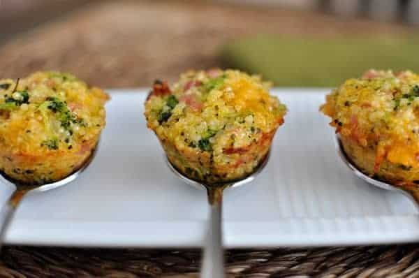 Three cooked mini cheese and broccoli quinoa bites on spoons.