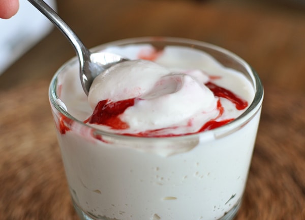 A glass goblet of homemade yogurt with a raspberry swirl and a spoon inside.