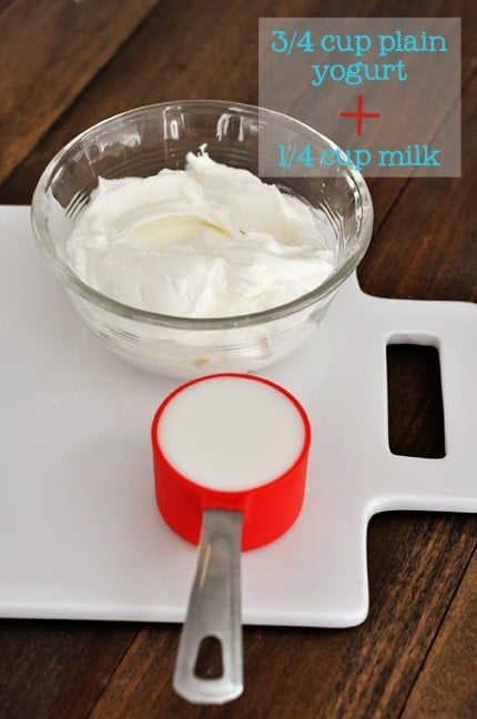 a white cutting board with a bowl of plain yogurt and a measuring cup of milk