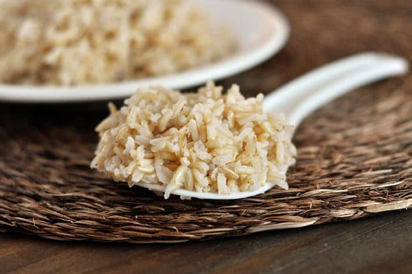 A spoonful of cooked brown rice with a plate of rice in the background.