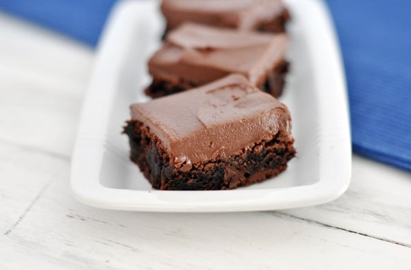 Top view of three chocolate frosted brownies on a white rectangular platter.