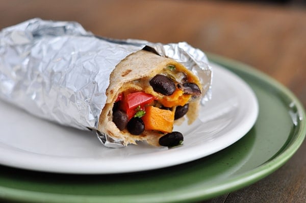 A tinfoil wrapped sweet potato and black bean burrito on a white plate.