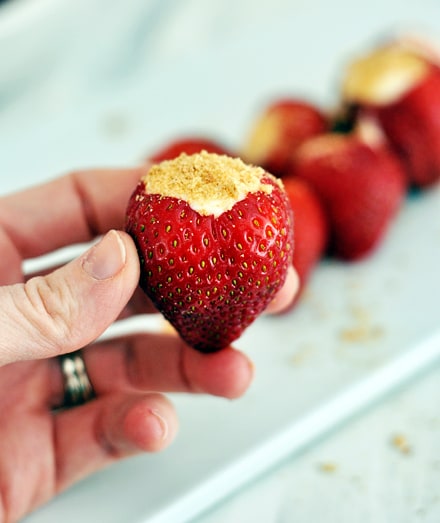 A hand holding a cheesecake stuffed strawberry with more strawberries in the background.