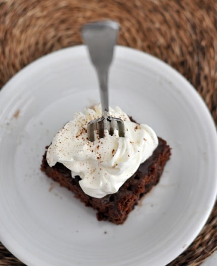 Top view of a whipped topping covered piece of chocolate cake with a fork sticking in it.